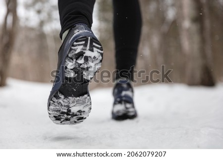 Winter exercise fitness lifestyle athlete walking with running shoes on snow and slippery ice needing traction soles on icy sidewalks. Run outside in cold weather. Royalty-Free Stock Photo #2062079207