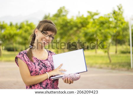 Lovely girl with glasses holding an open notebook.  Mixed race  European / Caucasian female student woman looking at camera.