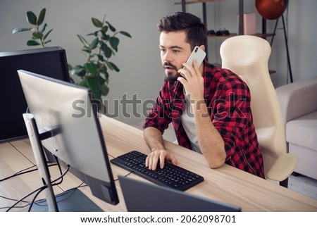 Photo of serious focused young man write computer programmer hold phone talk indoors inside office workplace