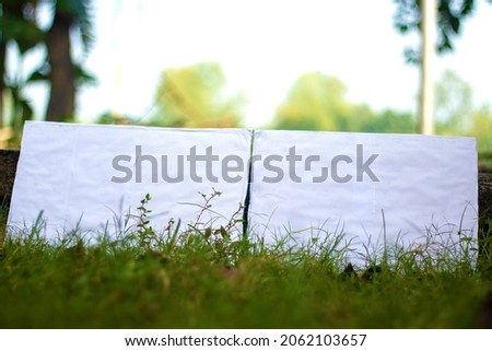 Two white blank signboards leaning against a small stone on the green grass for advertising by writing any text or design