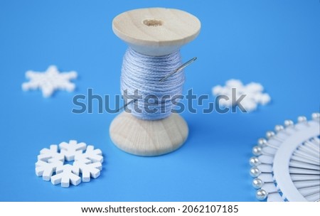 thread, snowflakes and needle on a blue background. Sewing accessories. Winter-themed sewing
