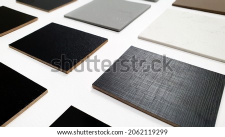 perspective view of multi surface of melamine samples in black color and multi color of grainy artificial stone samples for selection placed on white paper background (focused at fabric texture). Royalty-Free Stock Photo #2062119299