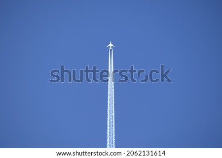 Distant passenger jet plane flying on high altitude on clear blue sky leaving white smoke trace of contrail behind. Air transportation concept. Royalty-Free Stock Photo #2062131614