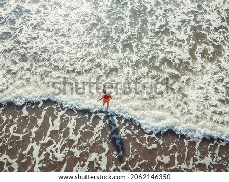 Top view from a drone of a young blonde woman standing on the seashore, waves enveloping her legs.Hot beach with cool waves.Concept of summer and relaxation,seascape with a girl, beach,beautiful waves