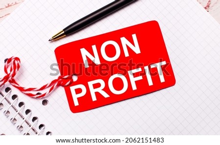 On a white notebook there is a black pen and a red price tag on a string with the text NON PROFIT