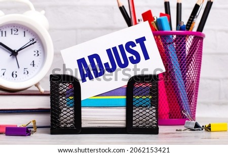 The office desk has diaries, an alarm clock, stationery, and a white card with the text ADJUST. Business concept.