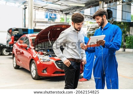 Mechanic show the car checking list for customer with blur his assistant checking red car. Focus on mechanic and customer on the right side. Auto car repair service center. Professional service. Royalty-Free Stock Photo #2062154825