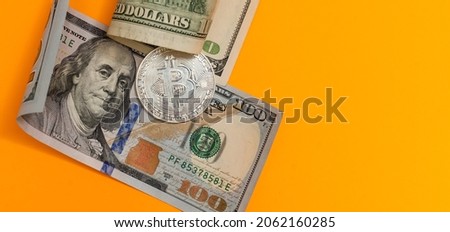 Golden and silver bitcoins and hundred dollar bills on wooden desk
