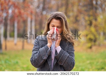 A girl stands on the street in a park in autumn and blows her nose in a handkerchief Royalty-Free Stock Photo #2062170272
