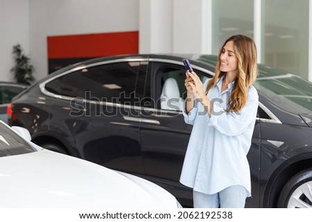 Woman customer female buyer client wears blue shirt do photo on mobile cell phone choose auto want buy new automobile in car showroom vehicle salon dealership store motor show indoor. Sales concept