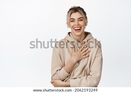 Young natural girl with white healthy smile, laughing and looking happy at camera, standing in beige hoodie over white background