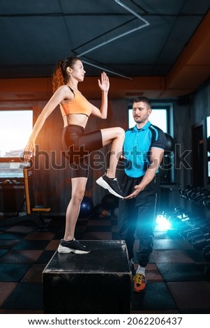 athlete female has exercising lunges on step box with personal trainer in gym