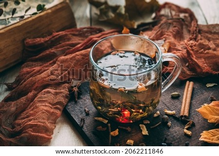 Glass mug with tea on a light wooden table on a dark board. Next to it is an old book and autumn leaves. View from above. Autumn mood