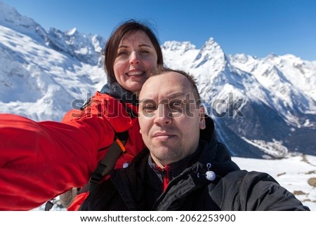 Dombay ski resort, a beautiful girl makes a selfie on the background of the Caucasus mountains, a happy couple makes a selfie on a smartphone on ski slopes when snowboarding in mountains.
