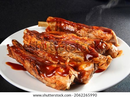 Steaming pork ribs with barbecue on a white plate and black background and a rim light Macro still life food photography