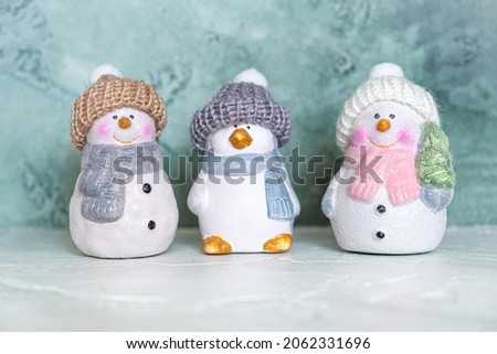Three ceramic New Year's toys - a penguin and snowmen in knitted hats and scarves on a turquoise background. New year and christmas concept. Greeting card.