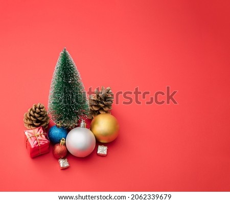 Minimal new year Christmas scene with tree, colorful baubles, presents and gift box on red pastel background.