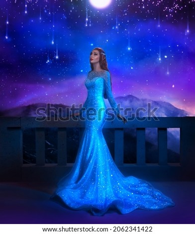 Photo with noise. Fantasy happy woman princess stands on balcony looks at night sky space stars. Girl enjoy magic starfall ball night sky. Elegant long shiny blue dress, train. Fairy Queen 
