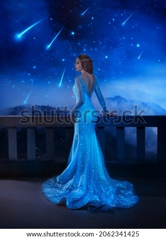 Photo with noise. Fantasy woman princess stands on balcony looks at night sky space cosmos falling stars. Girl enjoy magic starfall ball. Elegant long shiny blue evening dress . Fairy lady Queen.