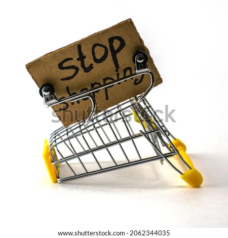 the concept of refusing to buy reasonable consumption is an inverted shopping cart on a white background next to a sign that says stop shopping. High quality photo