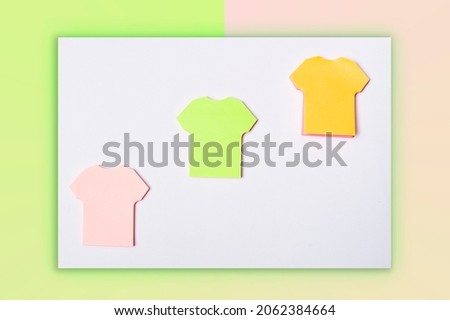 Yellow,Green and Pink t shirt shaped sticky notes, placed diagonally. Isolated on a white background with light pink and green borders