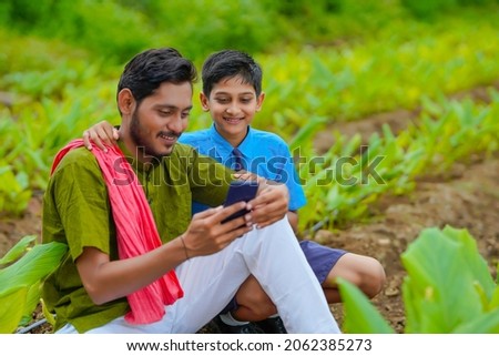 Indian farmer using smartphone with his child at green turmeric agriculture field.