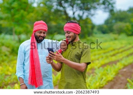 Indian farmer using smartphone at green turmeric agriculture field.