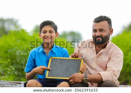 education concept : young indian farmer showing blank chalkboard with his child