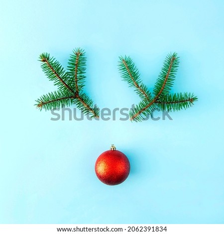 The reindeer Christmas face is made of Christmas tree twigs and a red Christmas tree decoration. On a pastel blue background. Creative New Year's composition. Copy space.
