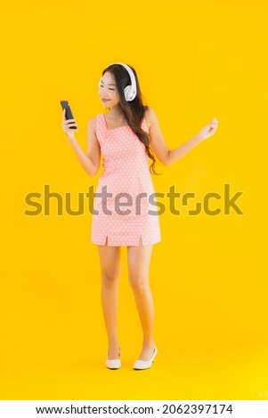 Portrait beautiful young asian woman listen music with smart mobile phone and headphone on yellow isolated background