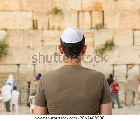 Back of a young tourist in casual clothes and kippah on the head looking at the wailing wall and religious praying near the sacred place of Judaism Royalty-Free Stock Photo #2062408508
