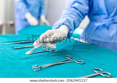 Nurse hand taking surgical instrument for group of surgeons at background operating patient in surgical theatre. Steel medical instruments ready to be used. Surgery and emergency concept Royalty-Free Stock Photo #2062441157