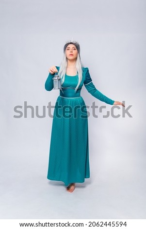 Full length portrait of a princess in a medieval, fantasy, turquoise dress with ash hair and a silver crown, posing with a lamp in her hands isolated on a white background.
