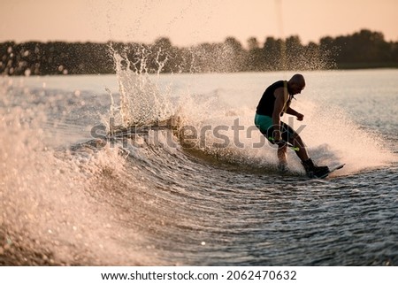 Athletic guy holds rope and riding wakeboard on splashing river wave. Active and extreme sports