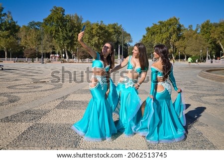 three belly dancers are taking a photo with their mobile phones. They are dressed in light blue and are having fun. Concept of friendship and happiness
