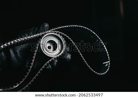 timing belt and tension roller in the hand of an auto mechanic on a black background, the concept of scheduled maintenance of the car, replacing the timing belt. Royalty-Free Stock Photo #2062533497