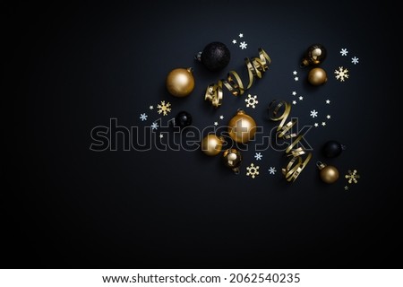 Christmas decorations in black and gold: Baubles, stars and ribbon on a black background. Table top view, flat lay, copy space.