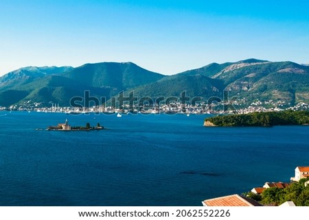 View of very small Our Lady of Mercy Island and Porto Montenegro Marina at background, located near Tivat city at foot of Vrmac mountain. Kotor bay of Adriatic sea. Montenegro. Blue summer landscape.