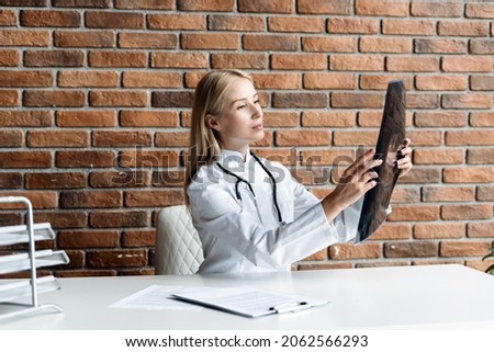 Concentrated and serious physician looking at x ray picture, diagnoses a patient injury. Doctor wearing in white coat uniform with stethoscope sitting in office at private clinic, checking mri scan