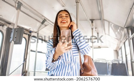 Woman Listening Music On Phone Riding In Bus. Portrait Of Stylish Smiling Girl Listening Music In Headphones, Using Smartphone While Riding In Public Transport. High Resolution.