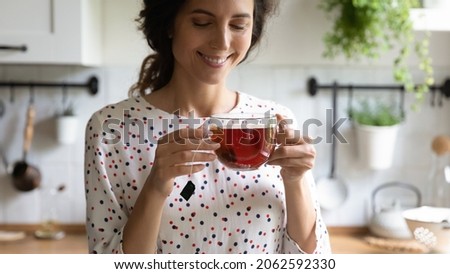 Happy woman taking tea break, holding glass mug, standing in kitchen, smelling and drinking hot aromatic beverage, enjoying morning and breakfast at home. Teatime, hygge, healthy lifestyle concept Royalty-Free Stock Photo #2062592330