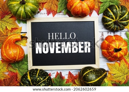 Hello November text on blackboard decorate with maple leaves and pumpkin on wooden background