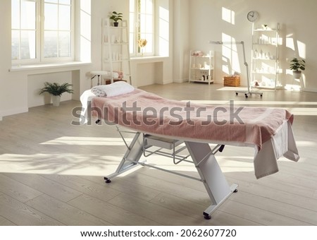 Interior of cosmetology clinic. Specialized couch for massage or cosmetic procedures in middle of bright beauty salon. Bright medical office with professional equipment and couch covered with towels. Royalty-Free Stock Photo #2062607720