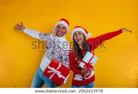 Close up photo of beautiful happy and excited young couple in love in Christmas clothes with gift boxes in hands while they celebrating New Year and giving presents yo each other