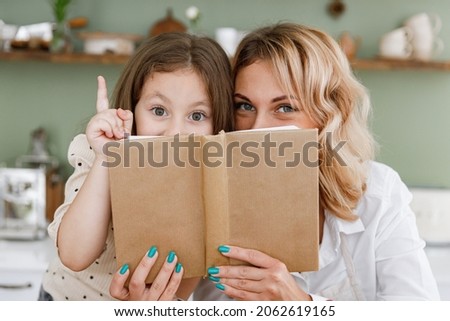 Chef cook baker mom woman in white shirt work baby girl helper read cookbook point finger up hide at kitchen table home Cooking food process concept Mommy little kid daughter prepare fruit sweet cake Royalty-Free Stock Photo #2062619165