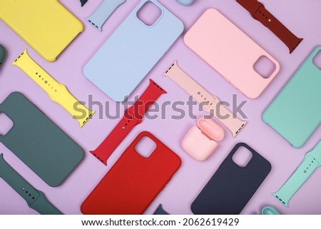 Colored silicone phone cases, complete with watch strap and case for headphones. Set. Up to date technology.Close up of diverse personal accessory laying on the lavender background. Flat lay Royalty-Free Stock Photo #2062619429