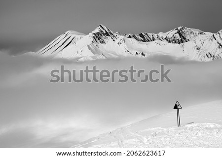 Black and white view on warning sing on ski slope and snowy mountains in fog. Caucasus Mountains at winter, Georgia, region Gudauri.