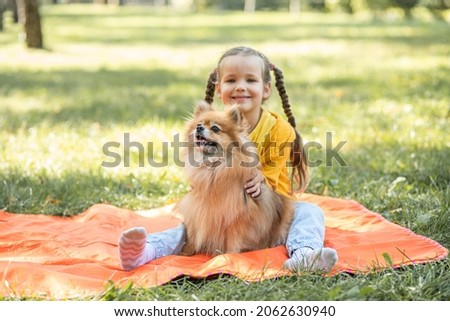 A girl with a Spitz dog, a small child is resting in the park with her pet, taking care of pets, a dog is a friend of man.
