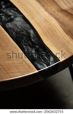 Expensive vintage furniture. The table is covered with epoxy resin and varnished. Luxury quality wood processing. Wooden table on a dark background. A black epoxy river in a round tree slab.