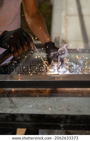 close-up of the hands of a person wearing black protective gloves while using a metal welding tool, sparks from the machine, machine manual work in the factory